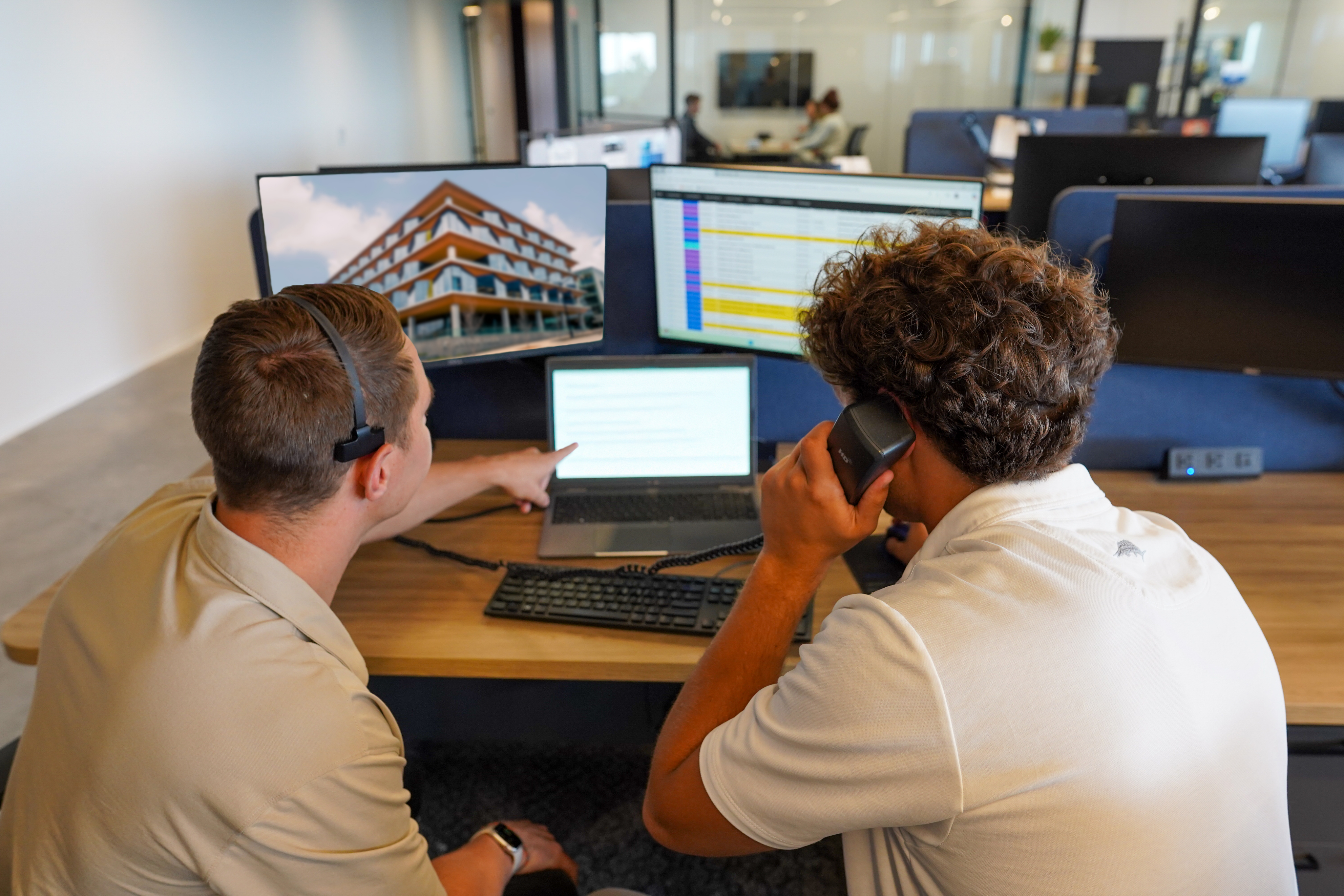 Two people on a phone call together with one of them pointing at a laptop screen